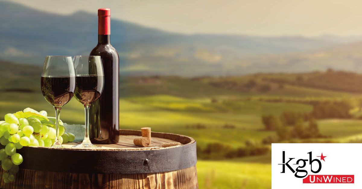 Scenic view of a wine bottle and two glasses on a barrel with lush green hills in the background.