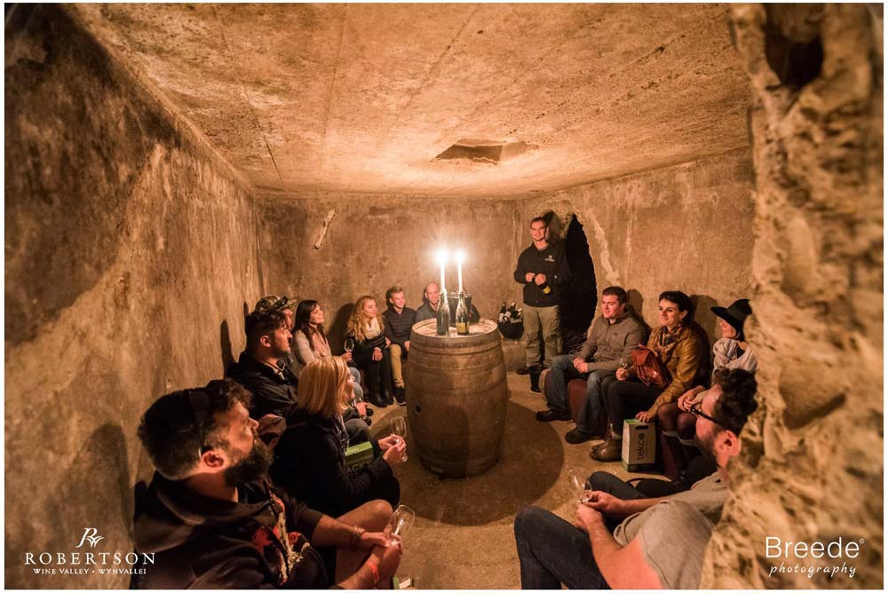 Group of people participating in a candlelit wine tasting in an underground cellar, creating a cozy and intimate atmosphere.