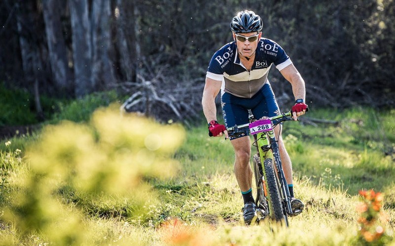 Focused male mountain biker racing through a lush forest trail, sporting a 'Bosch' jersey.